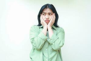 image of depressed beauty asian woman with dark hair holding her face with two palms looking away show worry face expression wear green oversized shirt isolated on white photo