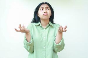 clueless asian woman with dark hair looking at camera with confusion expression raising two palms sideways wearing green oversized shirt, showing and presenting gesture, questioning, asking photo