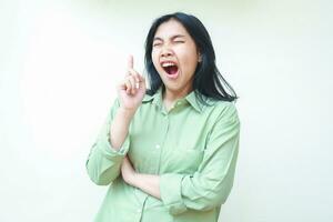 tired yawning asian woman pointing finger up to empty space and folding arms with eyes closed and mouth wide open just wakeup gesture wearing green oversiszed pajamas isolated on white photo