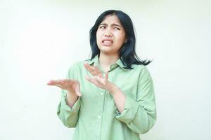 shocked asian woman with dark hair looking aside and raising palms showing disbelief face expression wearing green oversize shirt isolated on whtie background photo