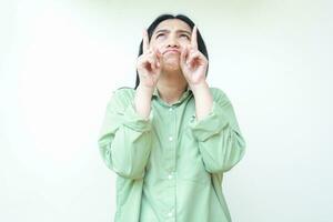 depressed asian woman with dark hair looking above and pointing up to empty space do showing presenting gesture wearing green oversized shirt standing isolated white background photo