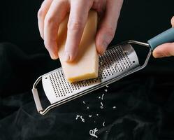 mano de el cocinar frota el queso en un rallador. foto