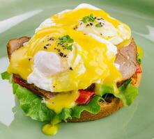 Tasty egg Benedict on green plate photo
