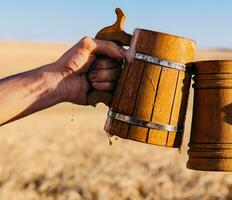 Hand with wooden beer clink mugs on the background of a field of wheat photo