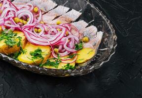 Sliced herring with baked potatoes and marinated onions on glass plate photo