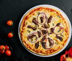 italian pizza with tomatoes, cheese, onions on black photo