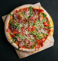 Italian pizza with prosciutto, arugula and tomatoes photo