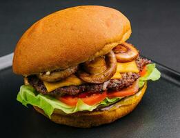 Burger with mushrooms and cutlet on black tray photo