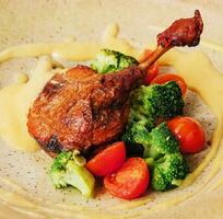 Confit duck leg with broccoli and tomatoes photo