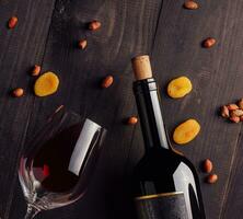 Glass and bottle of red wine with cheese, dried apricots and nuts photo