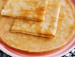 Stack of fresh thin pancakes on pink plate photo
