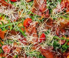 Italian pizza with prosciutto, arugula and tomatoes photo