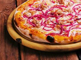 Pizza with tuna and red onion on wooden cutting board photo