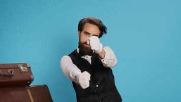 Blue background with optimistic bellhop dancing on audio tunes while he is using modern headset. Doorkeeper in classy suit showing groovy dance moves and behaving funky on camera. photo