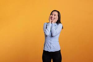 Carefree asian woman smiling in front of camera, posing with joyful expressions over in studio yellow background. Confident cheerful young adult feeling excited and happy enjoying good times photo