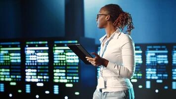 African american specialist strolling through server rows providing processing resources for different workloads. Experienced woman monitoring supercomputers tasked with solving complex operations photo