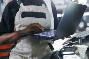 Mechanic in car service uses laptop to write invoice after repairing client automobile. Garage professional calculating final costs after refurbishing customer vehicle photo