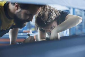 Precise mechanics in auto repair shop working together on fixing car, discussing best options. Teamworking employees collaborating on servicing broken vehicle, checking for fuel tank photo