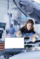 Mockup laptop with blurry background of serviceman changing old car gear oil with new one in repair shop. Isolated screen device and hardworking woman in garage using equipment to do vehicle checkup photo