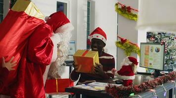 Revealing shot of manager dressed as Santa Claus spreading holiday joy in festive ornate office, offering presents to employees. Team leader surprising overjoyed company workers with Christmas gifts photo