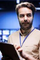 Vertical portrait of admin in cloud computing business with server racks used for computationally intensive tasks such as 3D rendering. Manager using tablet for yearly equipment inspection, close up photo