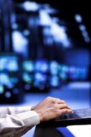 Serviceman using laptop to examine server rigs for power fluctuations, ensuring uninterrupted computing power. Employee monitoring data center, identifying potential bugs, close up photo