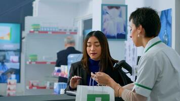 Customer in dispensary at checkout counter using credit card to buy pharmaceutical medication. Friendly client doing contactless purchasing in pharmacy after finding needed headache easing pills photo