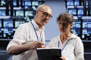 Elderly computer scientists monitoring data center racks, optimizing them for data processing requirements of AI applications. Supervisors oversee neural network server farm used for machine learning photo