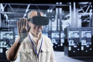 Octogenarian manager immersed in virtual reality at data center, doing equipment maintenance. Supervisor using VR headset to optimize server system performance, checking code lines photo