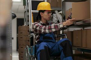 Storehouse employee in wheelchair taking cardboard box for order packing. Young asian choosing package on shelf and managing parcels transportation while working in inclusive workplace photo