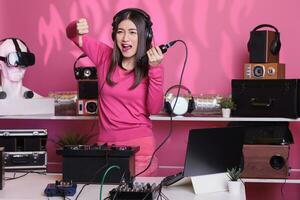 Unhappy artist holding microphone while doing disagreement gesture, expressing disagreement in studio over pink background. Dj woman performing song with electronics equipment and audio instrument photo