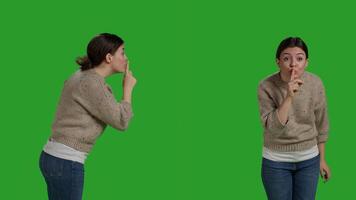 Private woman doing hush symbol to keep silence and secret over greenscreen backdrop, expressing privacy and secrecy on camera. Female model showing confidential and silent gesture, doing shh sign. photo