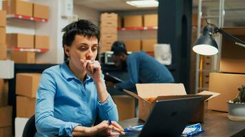 Woman employee analyzing goods from warehouse shelves, looking at merchandise in cardboard boxes before shipping goods order. Young adult working in storage space with supply chain. photo