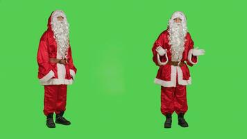 Santa claus create advertisement on camera for christmas eve holiday marketing, greenscreen studio. Saint nick embodiment pointing left and right to show something, winter celebration concept. photo