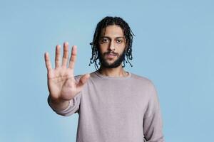 Arab man making stop gesture with hand and looking at camera with serious face expression portrait. Confident young person showing warning and rejection sign with arm concept photo