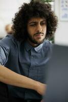 Young arab financial analyst analyzing statistics on laptop in business office. Company executive manager working at product promotional campaign and checking sales report photo