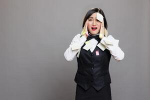 Overloaded stressed restaurant waitress with sticky notes on face and hands studio portrait. Overworked cafe employee in uniform having burnout, panicking and looking at camera photo