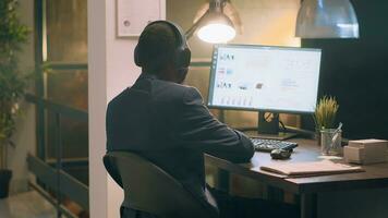 Employee enjoying music, bopping his head to rythm while solving company project tasks during nightshift. Bookkeeper in office with headphones on looking through financial business documents photo