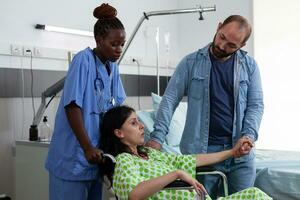 Gynecologist nurse helping pregnant woman to go to surgery in hospital ward. Patient with pregnancy sitting in wheelchair being comforting by husband and assistant in maternity facility photo