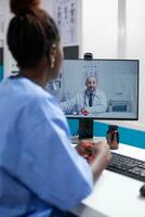 African american nurse at desk in a videocall communicating with doctor colleague in a professional medical office. Healthcare specialist doctor having online team meeting call with coworker photo