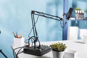 Sound controller console and professional microphone on table at empty blogger workspace. Audio mixer professional equipment on desk in vlogger home studio with no people photo