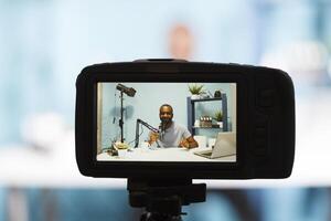 Blogger live streaming on online blog using professional camera closeup. Smiling african american vlogger recording video with videography equipment and speaking in microphone photo