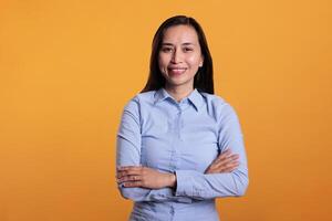 Portrait of smiling woman standing in arm crossed posing in studio over yellow background, smiling at camera during shoot. Cheerful filipino model with joyful expression having fun, enjoying free time photo