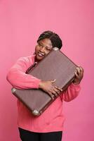 Cheerful model preparing suitcase baggage to leave on trip, travelling abroad to go on holiday vacation journey. Excited happy african american adult holding voyage luggage to do adventure. photo