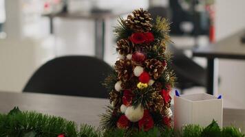 Close up shot on miniature Christmas pine tree decoration placed in empty startup office, with blurry background of festive workplace filled with xmas lights, garlands and wreaths photo