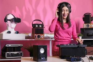 Cheerful musician standing at dj table mixing electronic music with techno using professional mixer console, having fun in studio over pink background. Artist playing stereo sounds with electronics photo