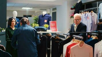 Customers choosing clothes from racks while doing purchases in fashion center during black friday discounts. Diverse obsessed people looking through clothing items on clearance, shopping. photo