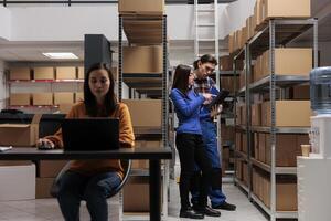 Warehouse workers managing inventory and comparing with report on digital tablet. Storehouse asian man and woman employees discussing parcels storing process optimization photo