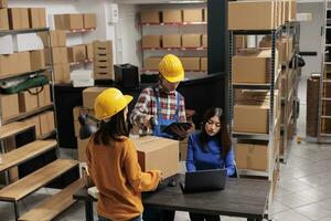 Storehouse managers team scanning parcel and checking information on laptop. Asian warehouse operators colleagues controlling cardboard box shipment at storage office desk photo