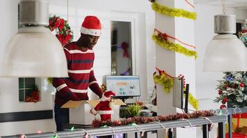 Disappointed worker in festive decorated office packs desk belongings on last day at work, consoled by coworker. Man getting fired from job during Christmas year end layoffs, clearing workstation photo